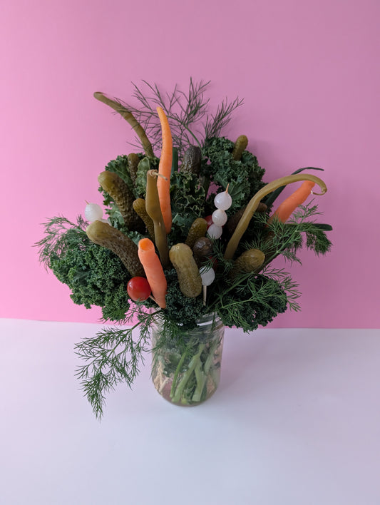 arrangement of pickles, styled like a bouquet of flowers in a mason jar, in front of a pink background